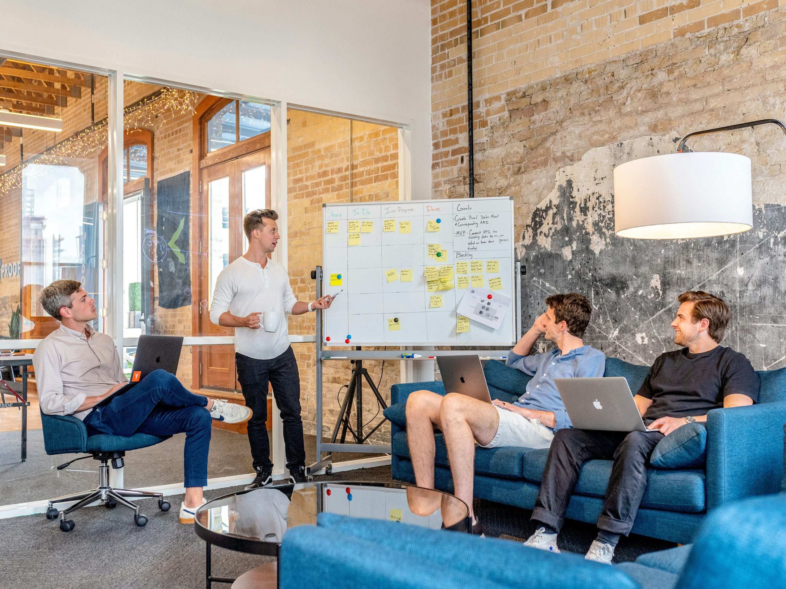 Group of professionals collaborating in a modern office setting, discussing a project with a whiteboard featuring sticky notes, laptops on their laps, and a focus on digital marketing strategies for home service businesses.