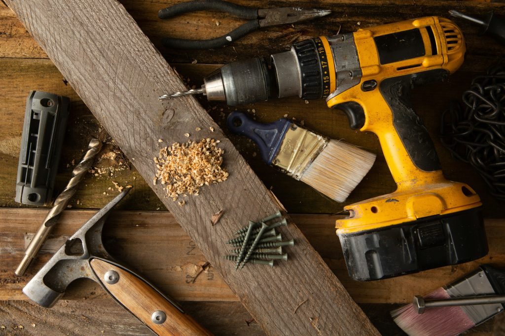 Power drill, wooden plank, paintbrush, and various tools arranged on a workbench, emphasizing home service business tools and DIY projects.